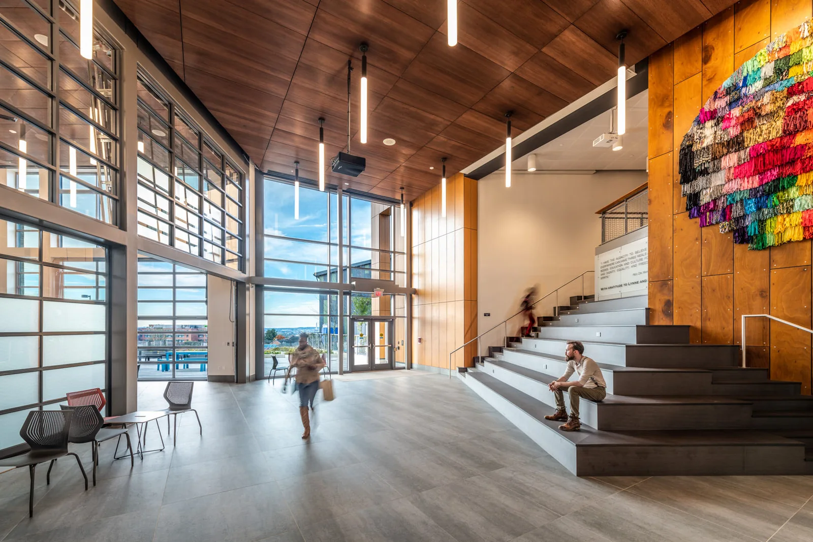 Wood ceiling panels and a tall wood-paneled wall above tiered seating in a bright gathering space.