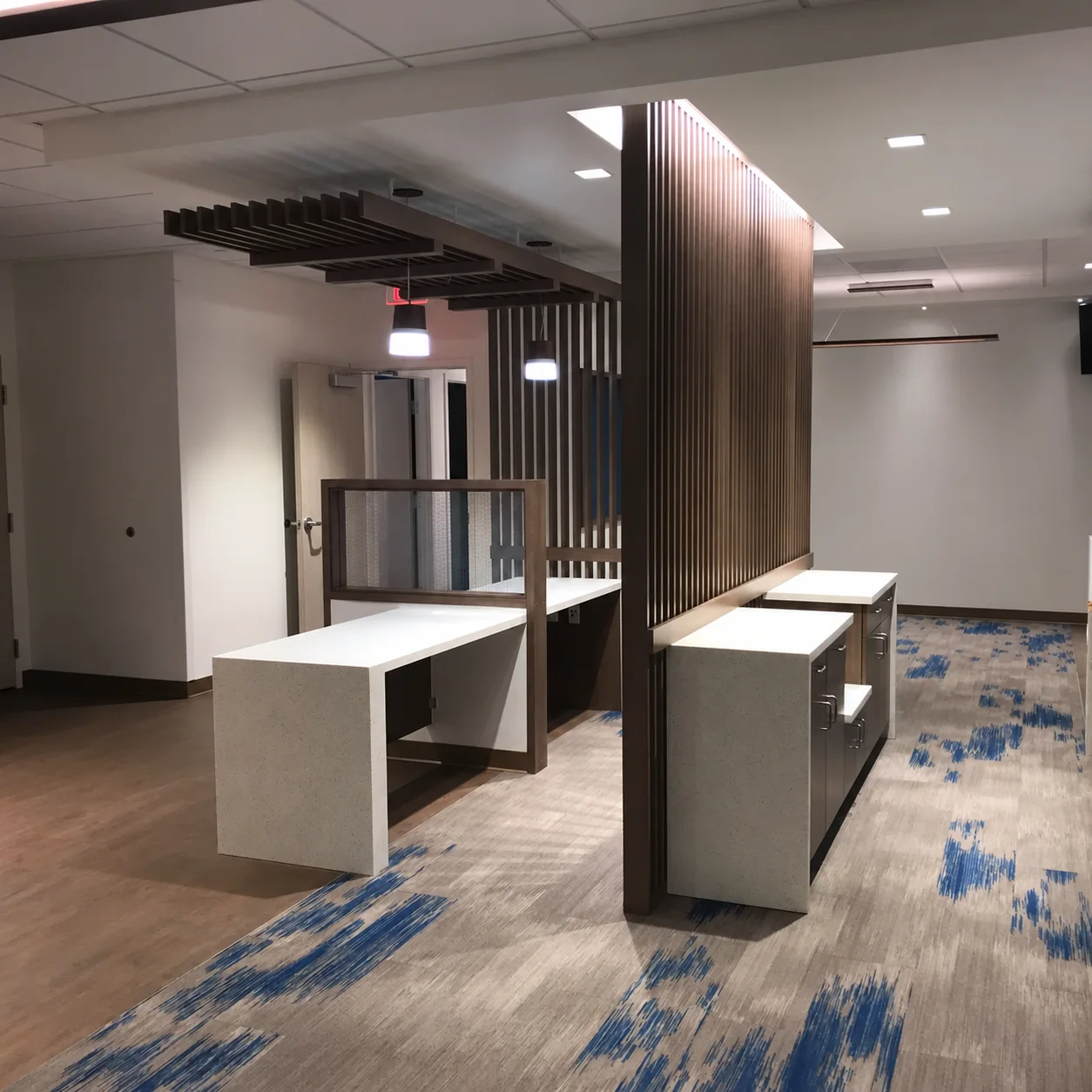 Wood slat partitions and overhead fins frame workstations with light countertops and base cabinets.