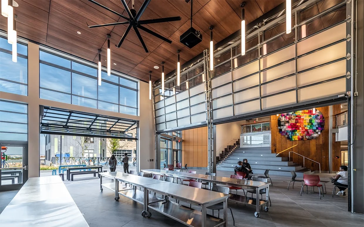 Completed gathering space with a wood ceiling, café tables and tiered seating.